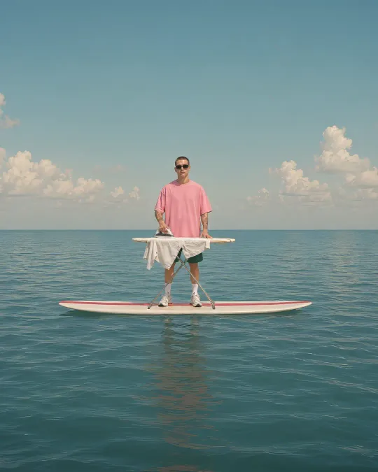 Sven stands on a board at sea with an ironing board and an iron.
